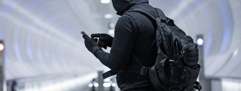 Hooded Lone wolf Man wearing black carrying bag in urban underground public transport setting